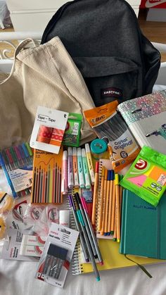 an assortment of school supplies including pencils, markers and pens on a bed with a backpack in the background