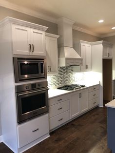 an empty kitchen with white cabinets and stainless steel appliances in the center, along with dark wood flooring