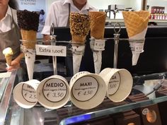 some ice cream cones are sitting on a glass shelf in front of two men behind the counter