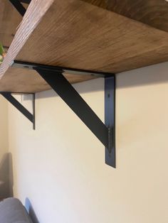 a wooden shelf with black metal brackets on it's sides and a plant in the corner