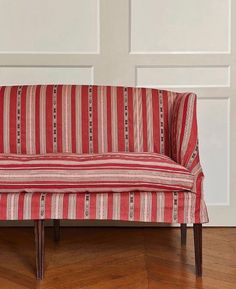 a red and white striped couch sitting on top of a hard wood floor next to a wall