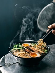 someone is holding chopsticks over a bowl of noodles with eggs and broccoli