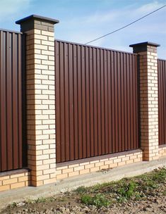 a brown brick fence with two pillars in front of it and grass on the side