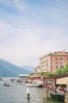 boats are docked in the water next to some buildings and mountains on either side of the lake