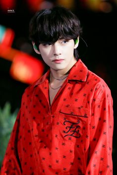 a man with black hair wearing a red shirt and green eyeliners on the runway