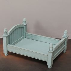 a small wooden bed sitting on top of a brown floor next to a white wall