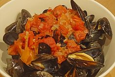 a white bowl filled with mussels on top of a wooden table