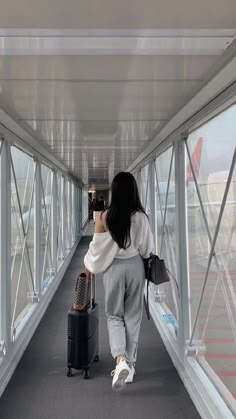 a woman walking down a walkway with her luggage and taking a photo on her cell phone