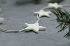 some white stars are hanging from a string on a table with pine needles and twine