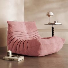 a pink chair sitting on top of a wooden floor next to a book and lamp