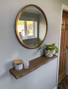 there is a mirror on the wall next to a shelf with candles and a potted plant