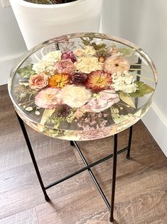 a glass table with flowers on it sitting next to a potted plant in the corner