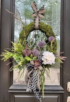 a wreath on the front door with flowers and greenery hanging from it's side