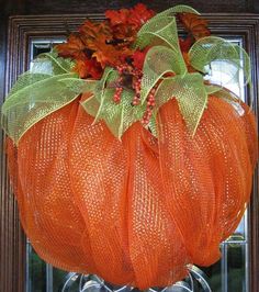 an orange mesh pumpkin with leaves and berries hanging from it's front door frame