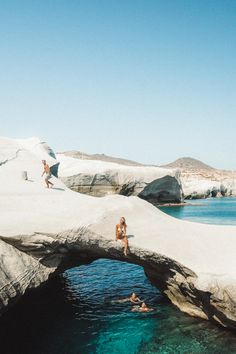 two people are swimming in the water near an arch shaped rock bridge that is made of concrete