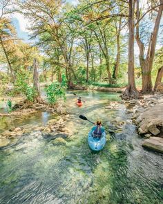 two people are kayaking down a river surrounded by rocks and trees in the woods