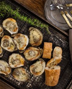 several oysters on a grill with bread and garnishes next to utensils