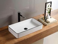 a white square sink sitting on top of a wooden counter next to a vase with flowers