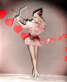 a woman in a red dress holding a bow and arrow with hearts flying around her