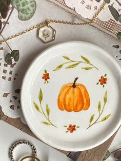 an orange pumpkin painted on a white plate with leaves and flowers around it, surrounded by other decorative items