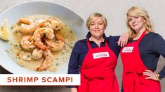 two women in red aprons standing next to a bowl of shrimp scampp