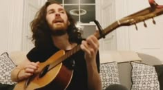 a man sitting on a couch holding a guitar in his right hand and looking up at the sky