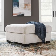 a white ottoman sitting on top of a rug in a living room next to a painting