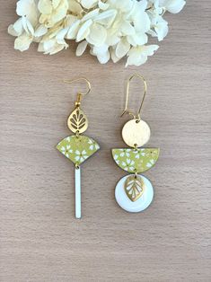 the earrings are made with gold, white and green leaves on them next to some flowers