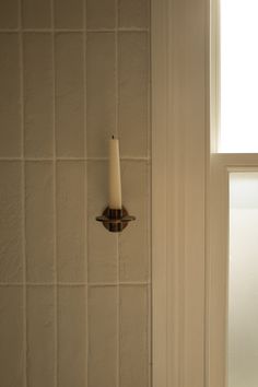 a candle that is on the side of a wall in front of a window with white tiles