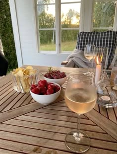 two glasses of wine on a wooden table with strawberries and chips in the bowl