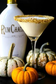 a martini glass filled with white wine and topped with an orange garnish next to mini pumpkins