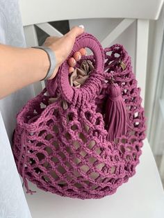 a hand holding a purple crocheted purse on top of a white chair with a pink handle