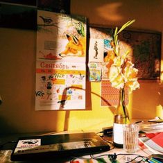 a vase with flowers in it sitting on a table next to a laptop and papers