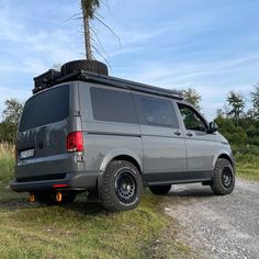 a grey van parked on the side of a dirt road next to a palm tree