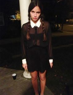 a young woman is standing on the sidewalk in front of a white pillar at night