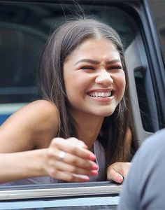 a smiling woman sitting in the drivers seat of a car with her hand out the window