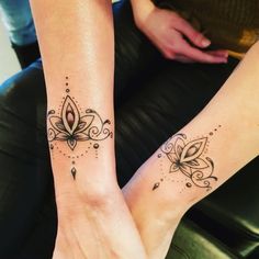 two people with matching tattoos on their legs sitting down together, one is holding the other's hand