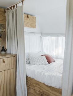 a bed with white sheets and pillows in a bedroom next to a wooden dresser under a window