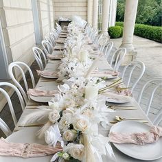 a long table is set with white flowers and place settings for dinner guests to sit at