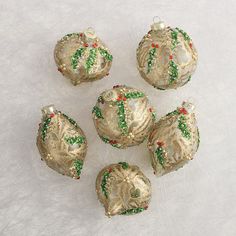 six gold and green christmas ornaments on a white surface