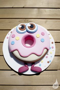 a pink cake with googly eyes sitting on top of a wooden table next to a white plate