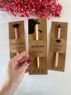 a person holding up some brown paper tags with graduation caps on them and two pencils in the middle