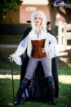 a woman dressed up as a witch with long blonde hair and black boots standing in the grass