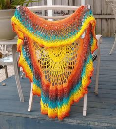 a colorful crocheted shawl sitting on top of a wooden deck next to chairs