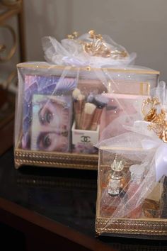 two clear boxes with various items in them on top of a black table and gold trimming around the edges