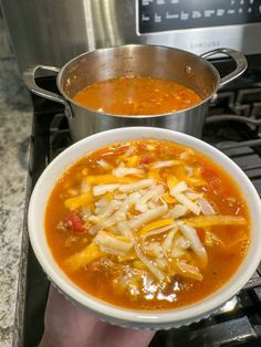 a person holding a bowl of soup in front of an open pot on the stove