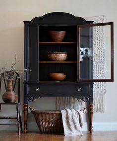 a black hutch with wooden bowls and baskets on it's shelves in front of a white wall