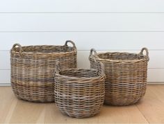 three wicker baskets sitting on top of a wooden floor next to a white wall