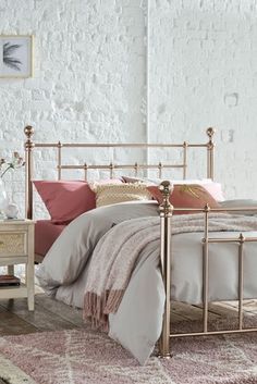 a white bed with pink pillows and blankets on it, next to a nightstand table