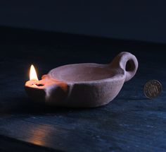 a lit candle sitting on top of a wooden table next to a small bowl filled with water